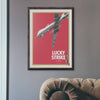 Lucky Strike It's Toast vintage poster art displayed above leather Chesterfield sofa in modern living room, political commentary wall art for contemporary home decor and masculine interior styling